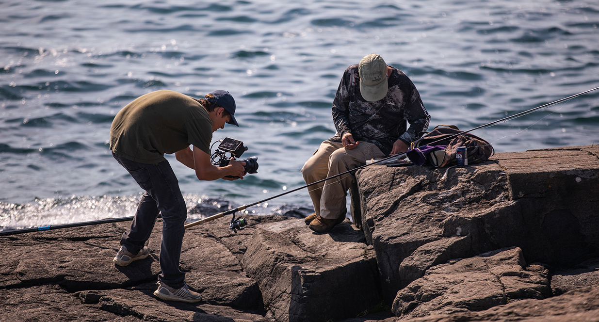 man fishing off the pier and man recording