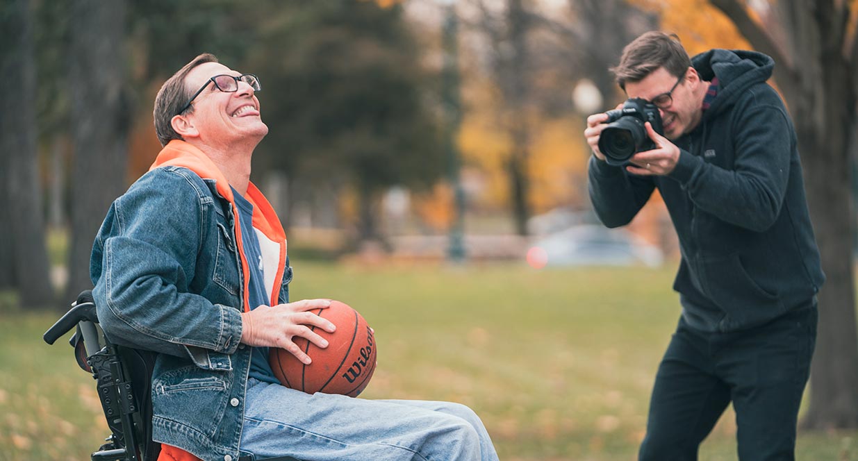 man in wheelchair playing basketball with a man taking a photo of him