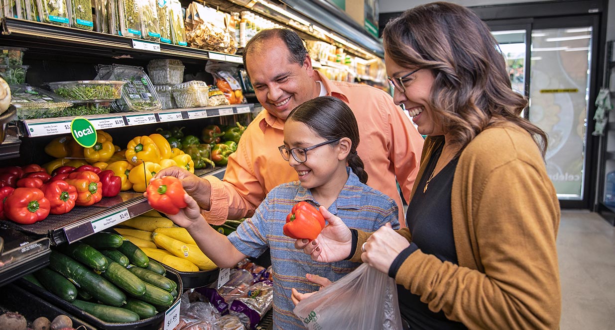 A man, woman and child shopping in the produce section of a grocery store