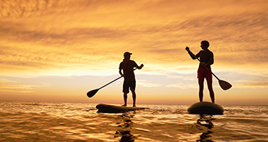 two people paddle-boarding at sunset